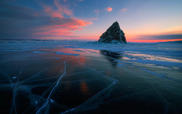 HD desktop wallpaper featuring a striking frozen landscape with a jagged ice formation on the horizon, under a vivid sunset sky filled with soft, colorful clouds. The ice has intriguing patterns and reflections.