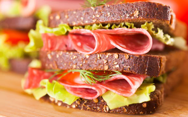 5K Ultra HD desktop wallpaper of a stacked deli sandwich: seeded rye, folded salami, crisp lettuce and herbs — food/sandwich background.