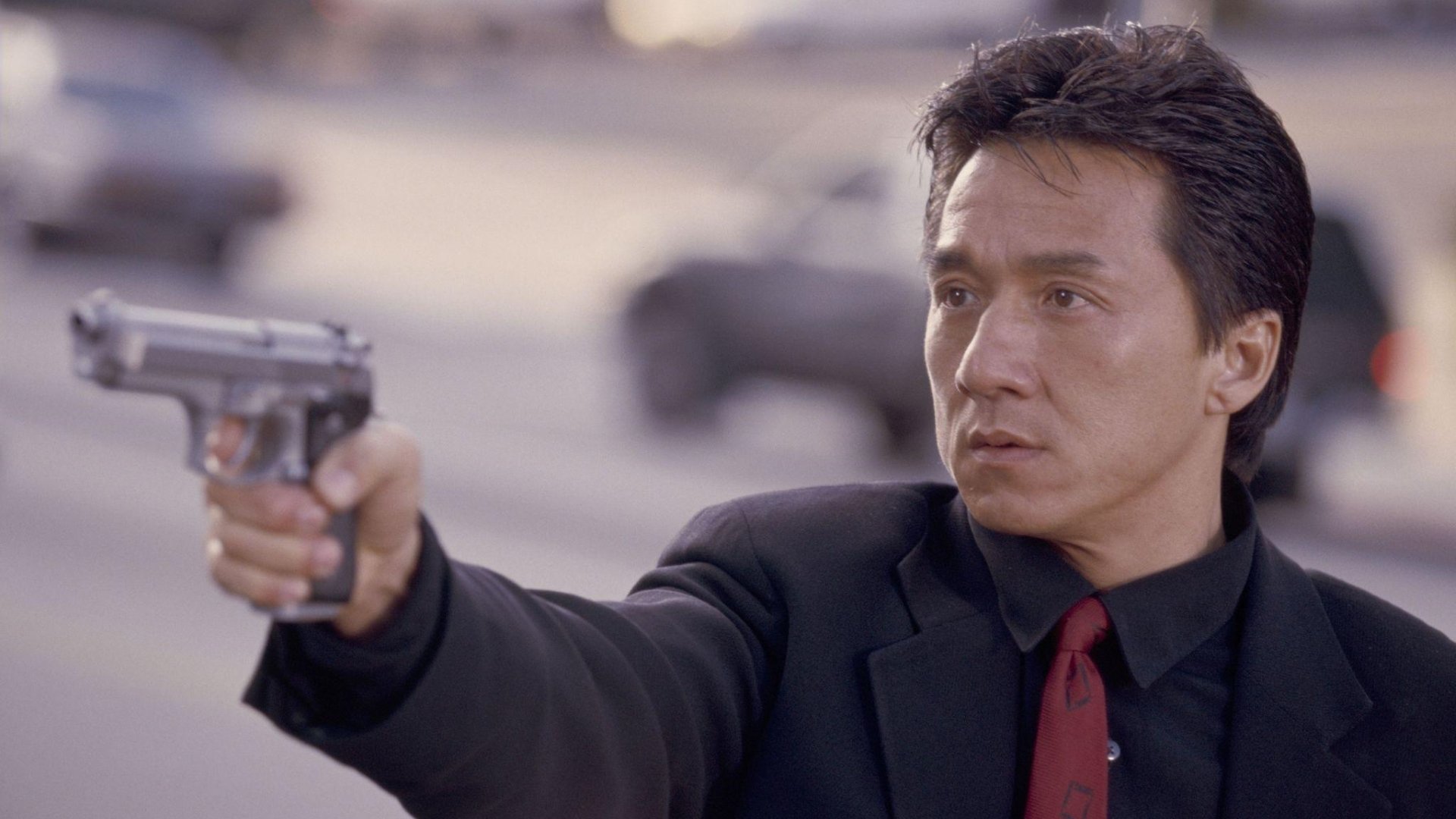 HD desktop wallpaper featuring Jackie Chan in a scene from the movie Rush Hour, holding a gun with a serious expression.