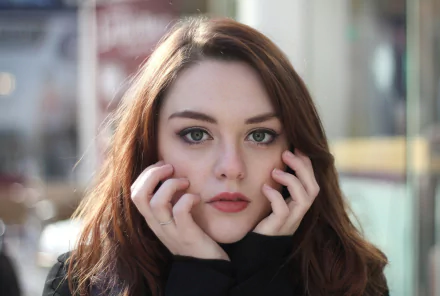 HD desktop wallpaper featuring a close-up portrait of a brunette woman with striking green eyes, gazing directly at the camera with her hands gently framing her face.