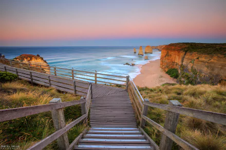 A wooden walkway and stairs lead down to the rocky cliffs and ocean shore of The Twelve Apostles along Victoria, Australia's coastline at sunset.