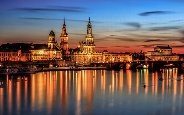 HD wallpaper featuring a night view of Dresden, Germany, with illuminated buildings and a bridge reflecting on the river. The city skyline is beautifully lit against a twilight sky.
