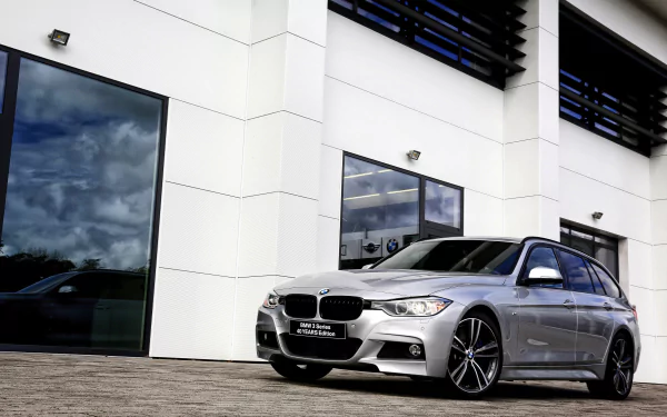Silver BMW 3 Series parked beside a modern white building, sporty car captured as a 2K Quad HD PC desktop wallpaper/background.