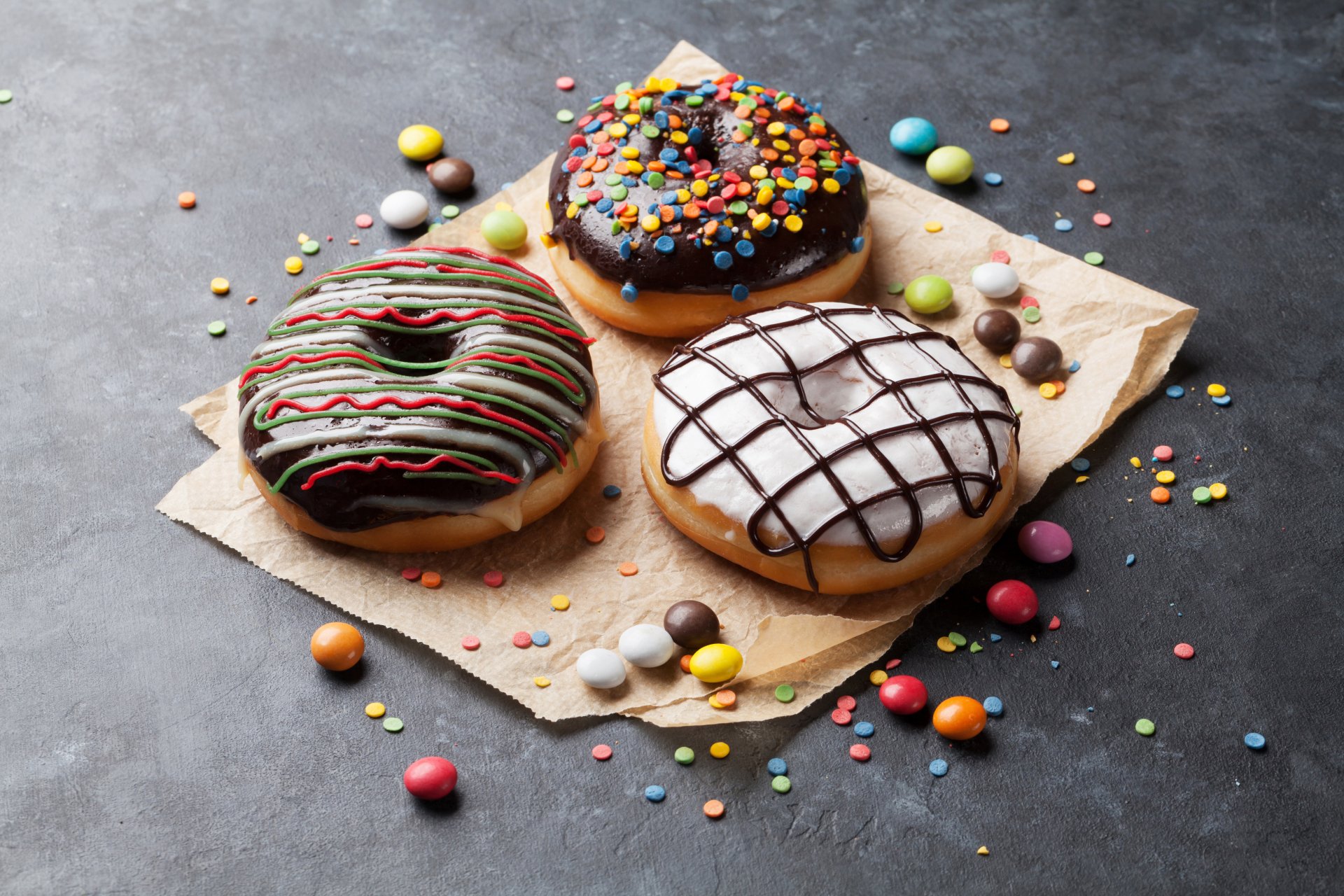 A vibrant 4K Ultra HD still life of colorful candy and three decorated doughnuts on parchment, set against a dark textured background.