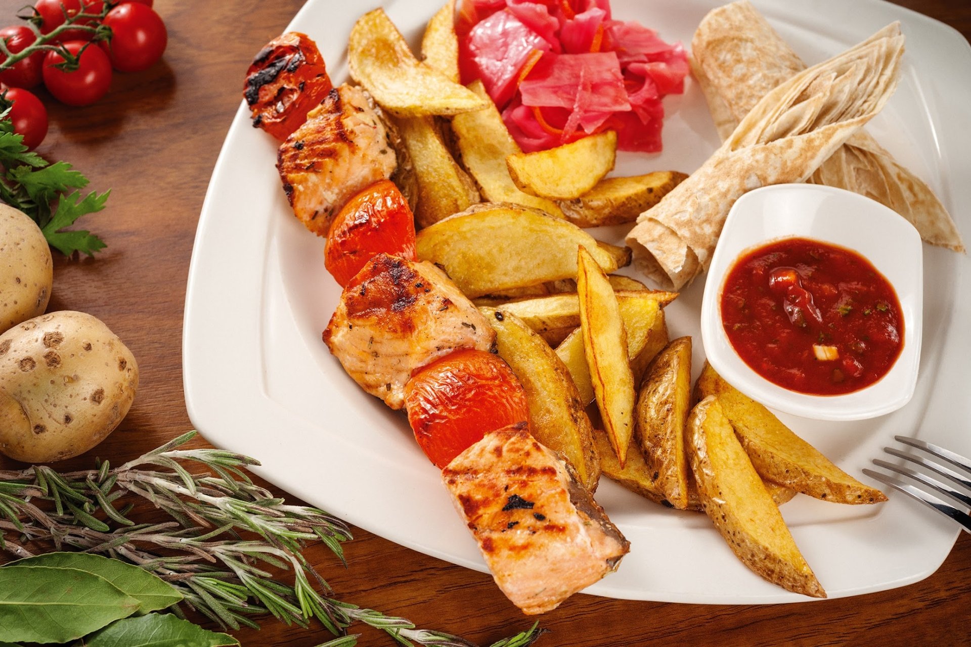 HD desktop wallpaper of a barbecue meal featuring grilled meat skewers, golden potato wedges, flatbreads, and a side of red dipping sauce on a white plate.