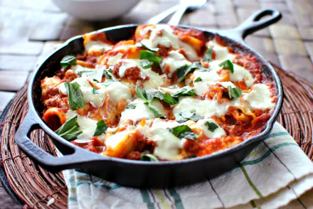 HD desktop wallpaper of a skillet filled with cheesy lasagna garnished with fresh basil leaves, showcasing a delicious meal.