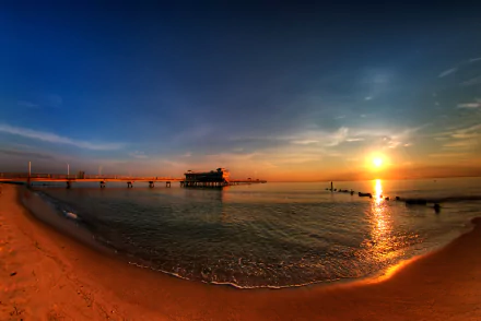 HD desktop wallpaper featuring a serene sunset over a calm ocean with a pier extending out to the horizon, capturing the tranquil beauty of the beach and sea.