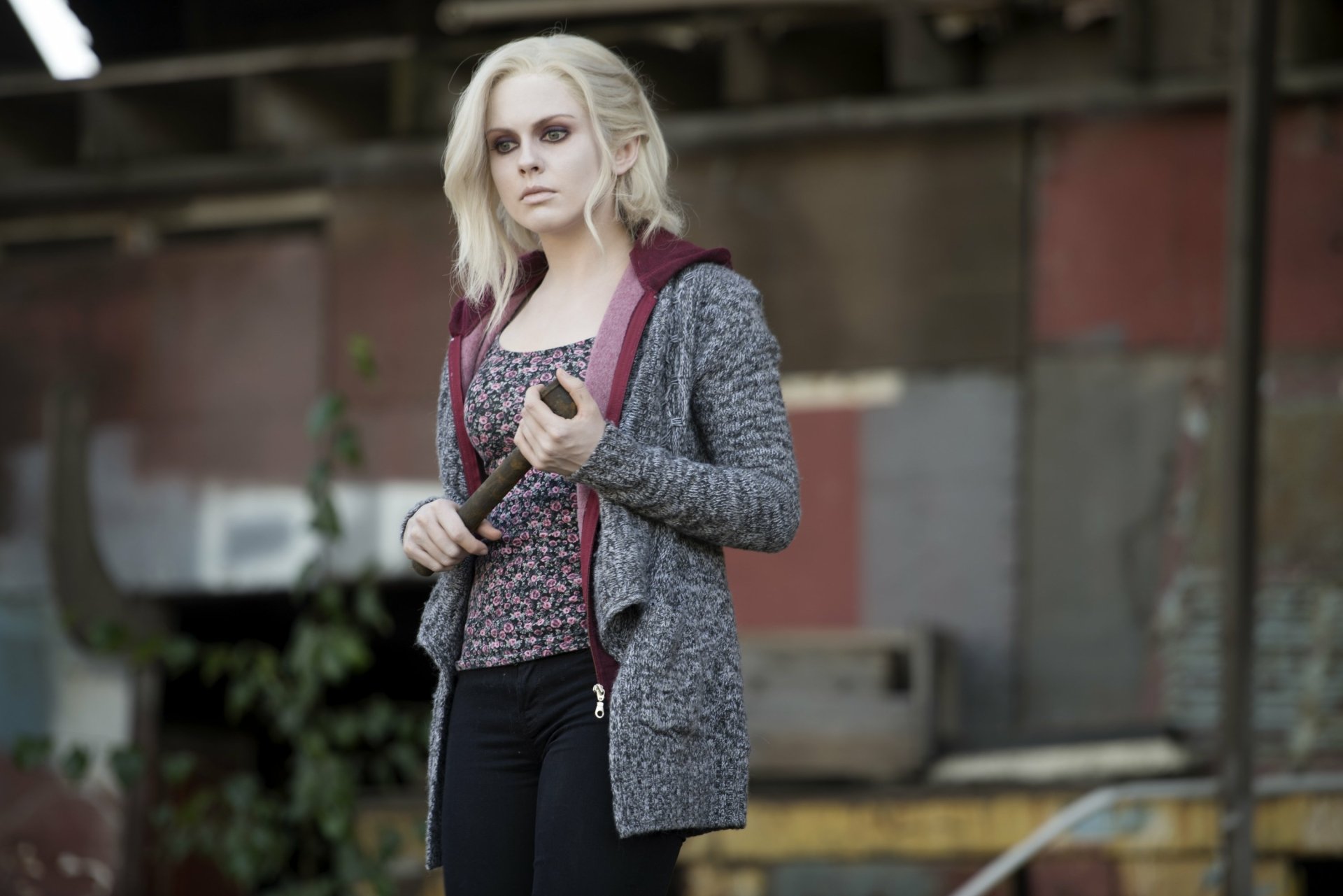 Pale young woman in a hoodie and patterned top holds a bat in an abandoned industrial lot — TV show character wallpaper, 2K Quad HD desktop background.