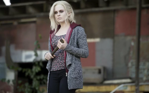 Pale young woman in a hoodie and patterned top holds a bat in an abandoned industrial lot — TV show character wallpaper, 2K Quad HD desktop background.