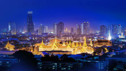 Night view of Bangkok cityscape featuring illuminated Grand Palace and modern skyscrapers under a clear sky, showcasing Thailand's blend of tradition and urban life.