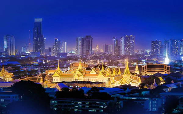 Night view of Bangkok cityscape featuring illuminated Grand Palace and modern skyscrapers under a clear sky, showcasing Thailand's blend of tradition and urban life.