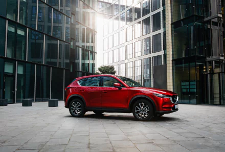 Red Mazda CX-5 SUV parked in a glass-walled urban plaza, shown as a 2K Quad HD PC desktop wallpaper background.