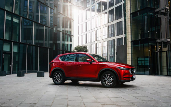 Red Mazda CX-5 SUV parked in a glass-walled urban plaza, shown as a 2K Quad HD PC desktop wallpaper background.