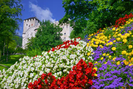 A vibrant spring scene in Tyrol, Austria, featuring a castle behind a colorful garden of purple, yellow, red, and white flowers in 4K Ultra HD.