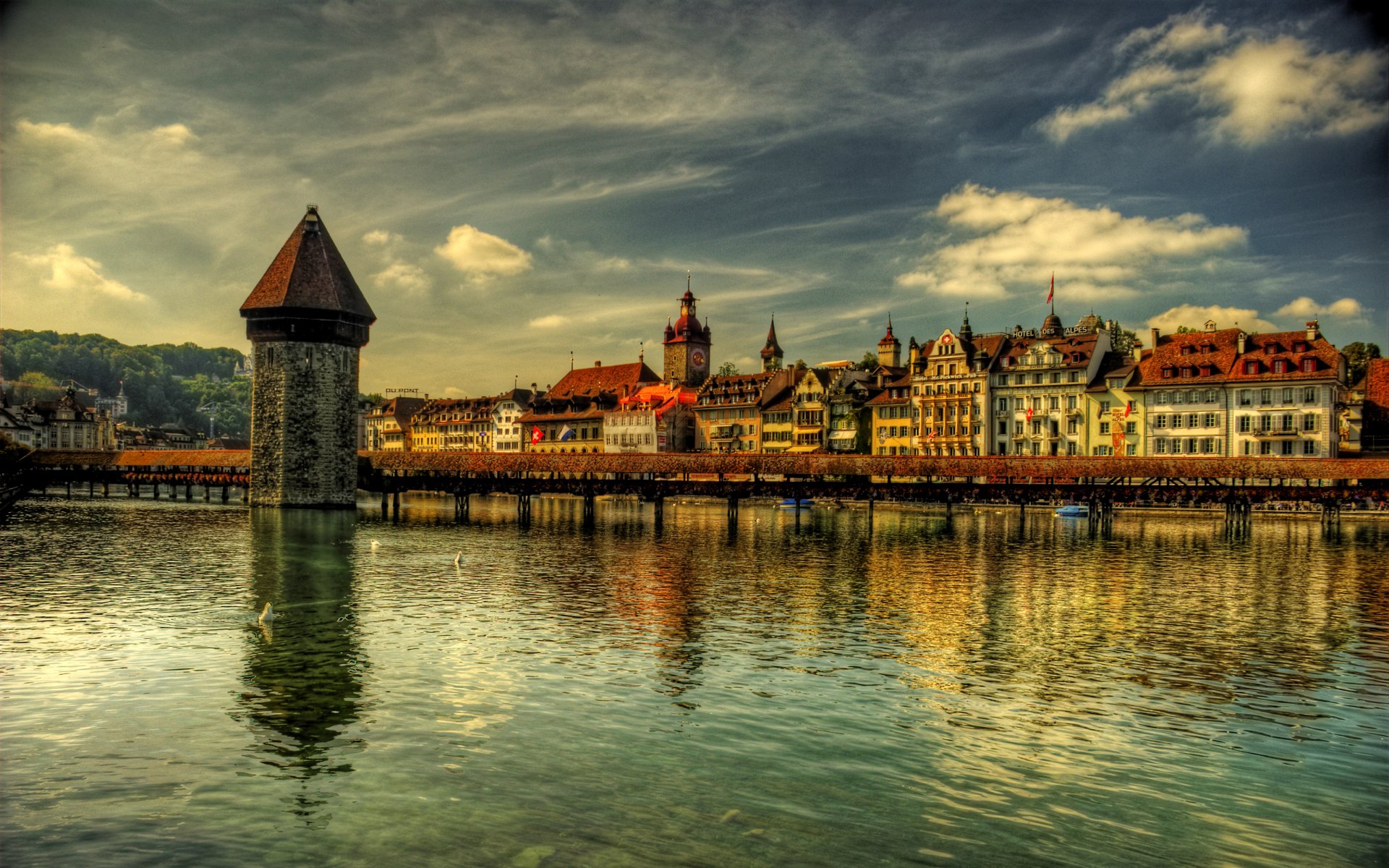 2K Quad HD wallpaper of Lucerne waterfront: historic man-made tower and colorful buildings reflected in calm water under a dramatic sky.
