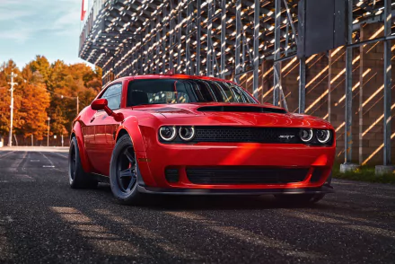 HD desktop wallpaper featuring a red Dodge Challenger SRT Demon, a powerful muscle car from Mopar, parked under a modern architectural structure with autumn trees in the background.