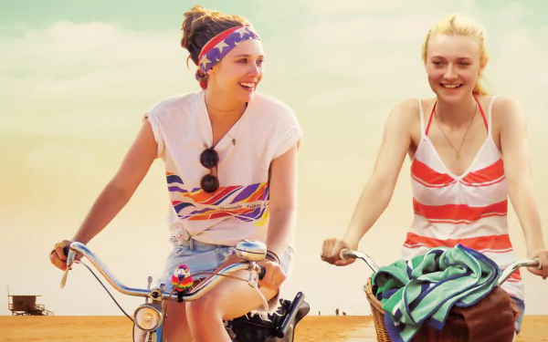 Elizabeth Olsen and Dakota Fanning riding bikes smiling in a scene from the movie Very Good Girls, featured as an HD PC desktop wallpaper and background.