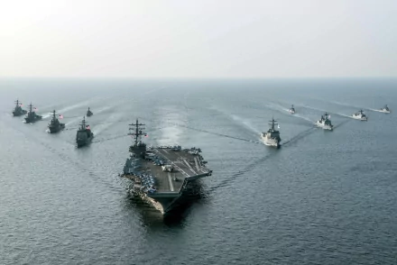 HD desktop wallpaper featuring the USS Ronald Reagan (CVN-76) aircraft carrier leading a naval fleet on the ocean horizon under a clear sky.