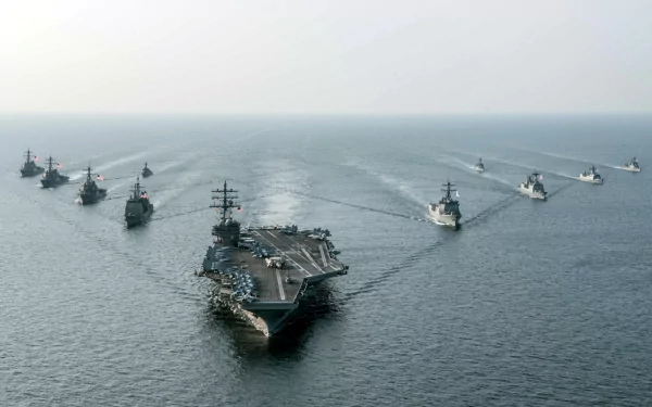 HD desktop wallpaper featuring the USS Ronald Reagan (CVN-76) aircraft carrier leading a naval fleet on the ocean horizon under a clear sky.