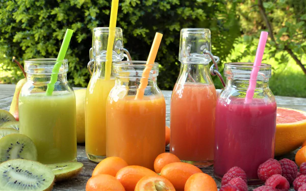 HD desktop wallpaper showing colorful fruit smoothies in glass bottles with straws, surrounded by fresh kiwi, raspberries, and kumquats in an outdoor setting.