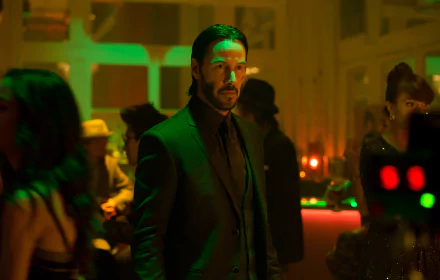 Keanu Reeves as John Wick stands in a dimly lit club with green lighting, surrounded by people. This HD desktop wallpaper captures an intense moment from the movie, featuring the iconic character in a moody setting.