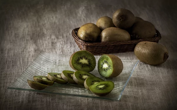 Close-up of fresh kiwi fruit, both whole and sliced, arranged on a glass plate and in a woven basket, captured in stunning 4K Ultra HD for PC desktop wallpaper.