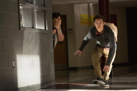Jacob Batalon and Tom Holland as Peter Parker in a scene from Spider-Man: Homecoming. They are sneaking through a hallway, with Batalon peeking from behind a corner and Holland crouched and alert.
