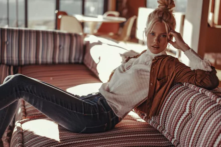 HD PC desktop wallpaper: fashion model woman reclining on a patterned sofa in warm sunlight, wearing a jacket and jeans, relaxed editorial vibe.