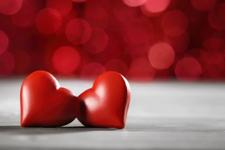 5K Ultra HD PC desktop wallpaper: two red hearts on a surface with artistic red bokeh background, love-themed heart image.