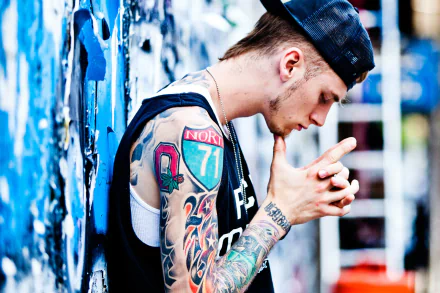 HD wallpaper featuring a person with tattoos, styled in a black outfit and cap, against a graffiti backdrop.