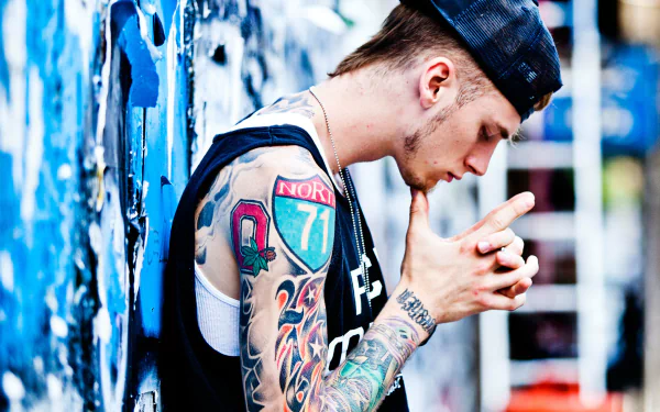 HD wallpaper featuring a person with tattoos, styled in a black outfit and cap, against a graffiti backdrop.