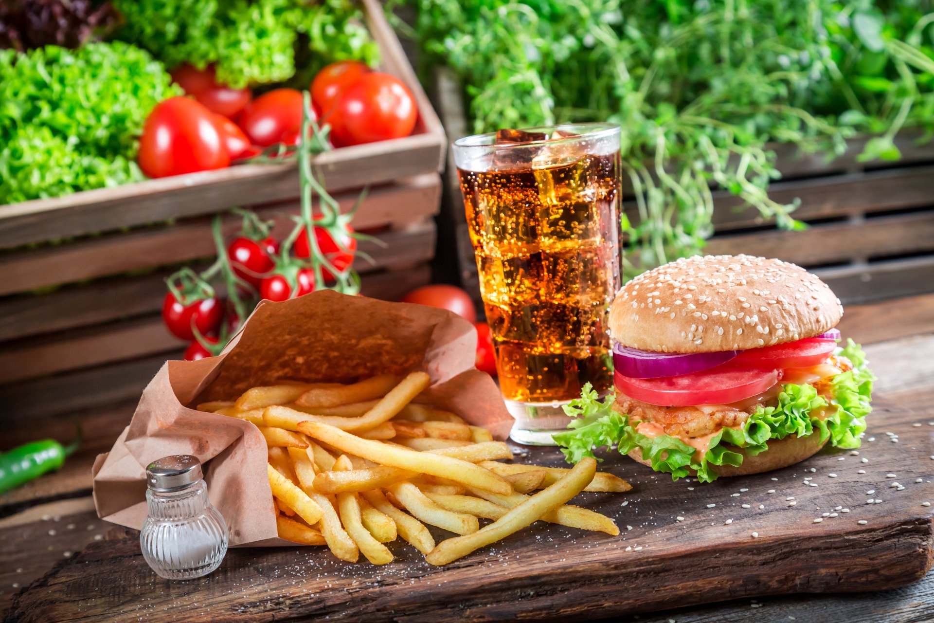 A 4K Ultra HD still life of a classic burger, crispy French fries, and a fizzy drink served on a rustic wooden surface with fresh vegetables in the background.