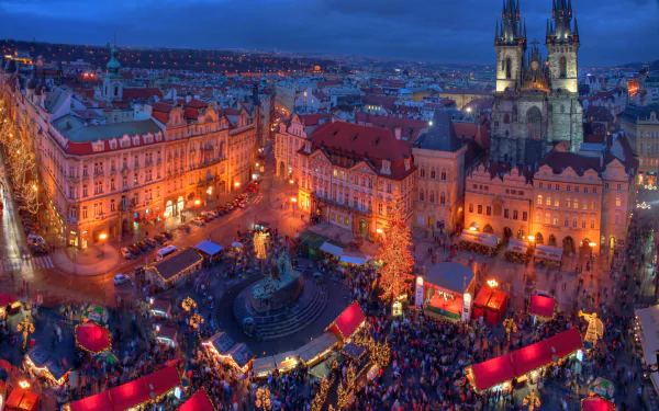 Nighttime cityscape of Prague's Christmas market in the Czech Republic, illuminated with festive lights and bustling crowds, captured in HD for a desktop wallpaper.