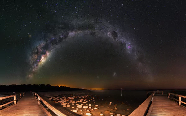4K Ultra HD night photography of a star-filled sky with the Milky Way arching over a wooden boardwalk and rocky shoreline.