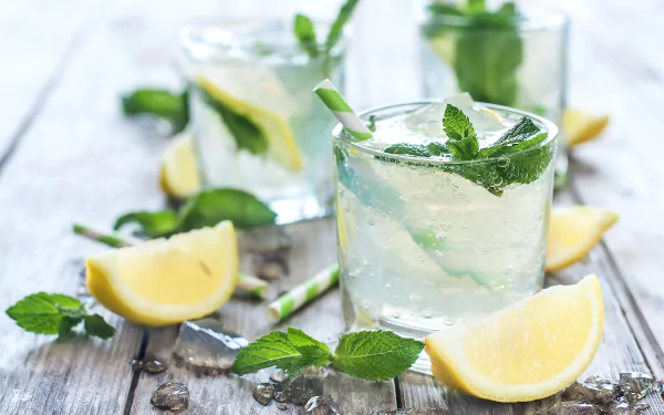 HD desktop wallpaper featuring a refreshing still life of a glass with lemon, mint leaves, and ice on a rustic wooden surface.