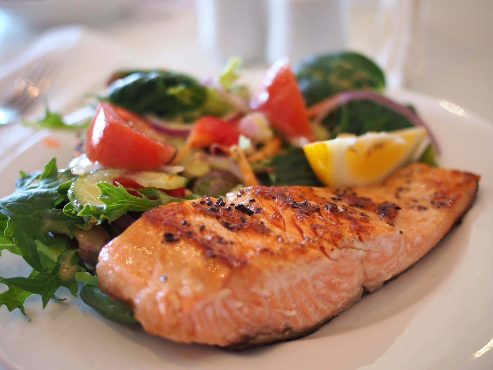 Close-up of a grilled salmon meal with fresh salad on a blurred background, showcased as an HD seafood desktop wallpaper.