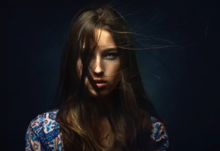 HD desktop wallpaper of a brunette model with striking blue eyes, her face partially shadowed against a dark background.