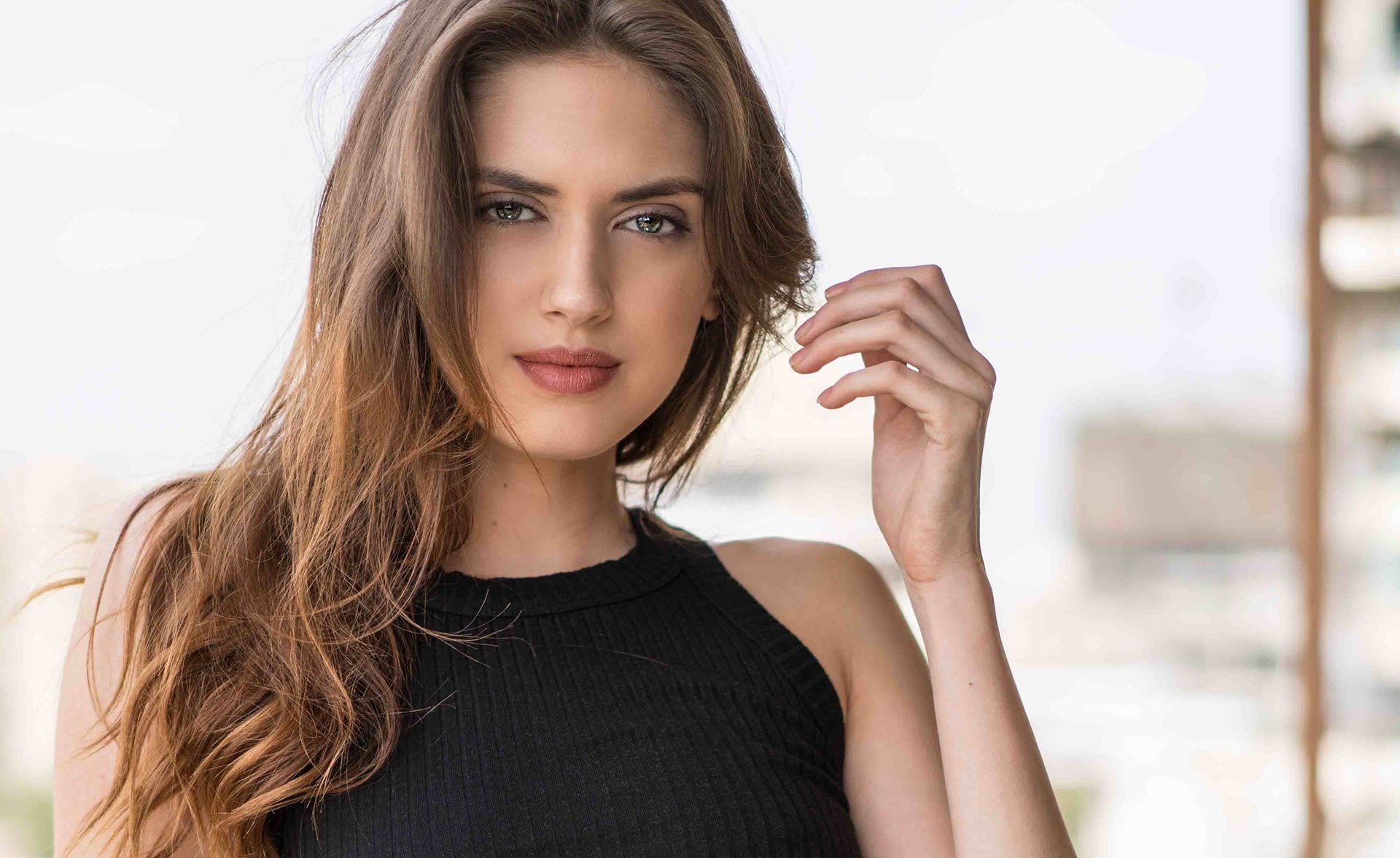 HD wallpaper featuring a brunette woman and model with long hair, gazing confidently at the camera. The background is slightly blurred, highlighting her face.