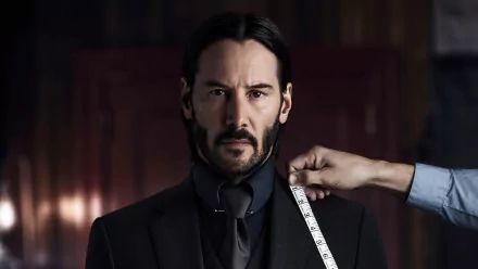 HD desktop wallpaper featuring Keanu Reeves as John Wick from John Wick: Chapter 2. The image shows him getting measured for a suit, emphasizing the film's stylish and intense look.