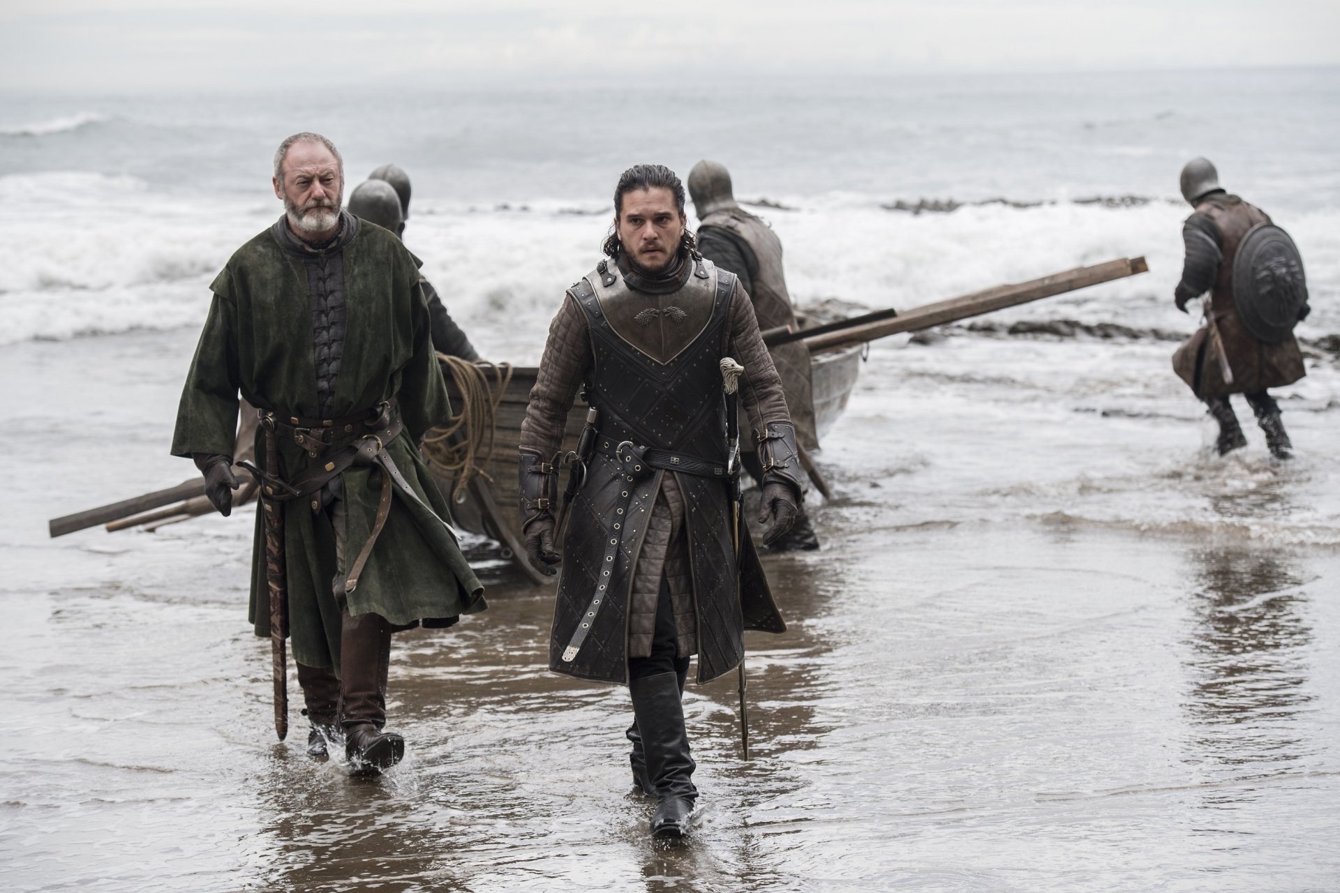 Game of Thrones: Jon Snow and Davos Seaworth stride ashore from a skiff on a gray, wet beach — 2K Quad HD desktop wallpaper.
