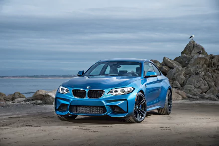 Blue BMW M2 car parked on a rocky beach under a cloudy sky, captured in 4K Ultra HD as a PC desktop wallpaper and background.
