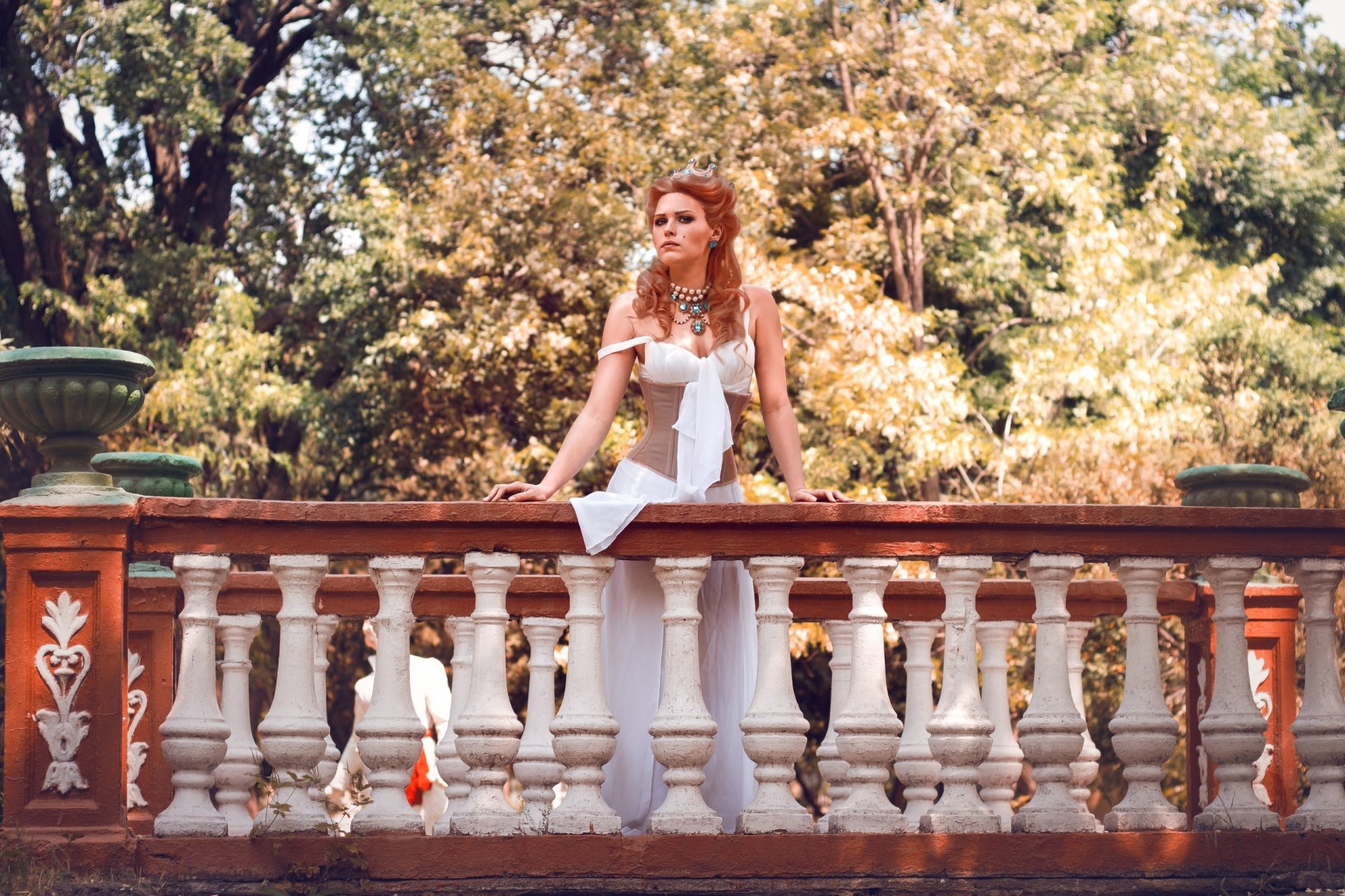 Cosplayer as Anna Henrietta from The Witcher 3: Wild Hunt in a white gown leaning on an ornate stone balustrade amid sunlit trees; 2K Quad HD PC desktop wallpaper/background.