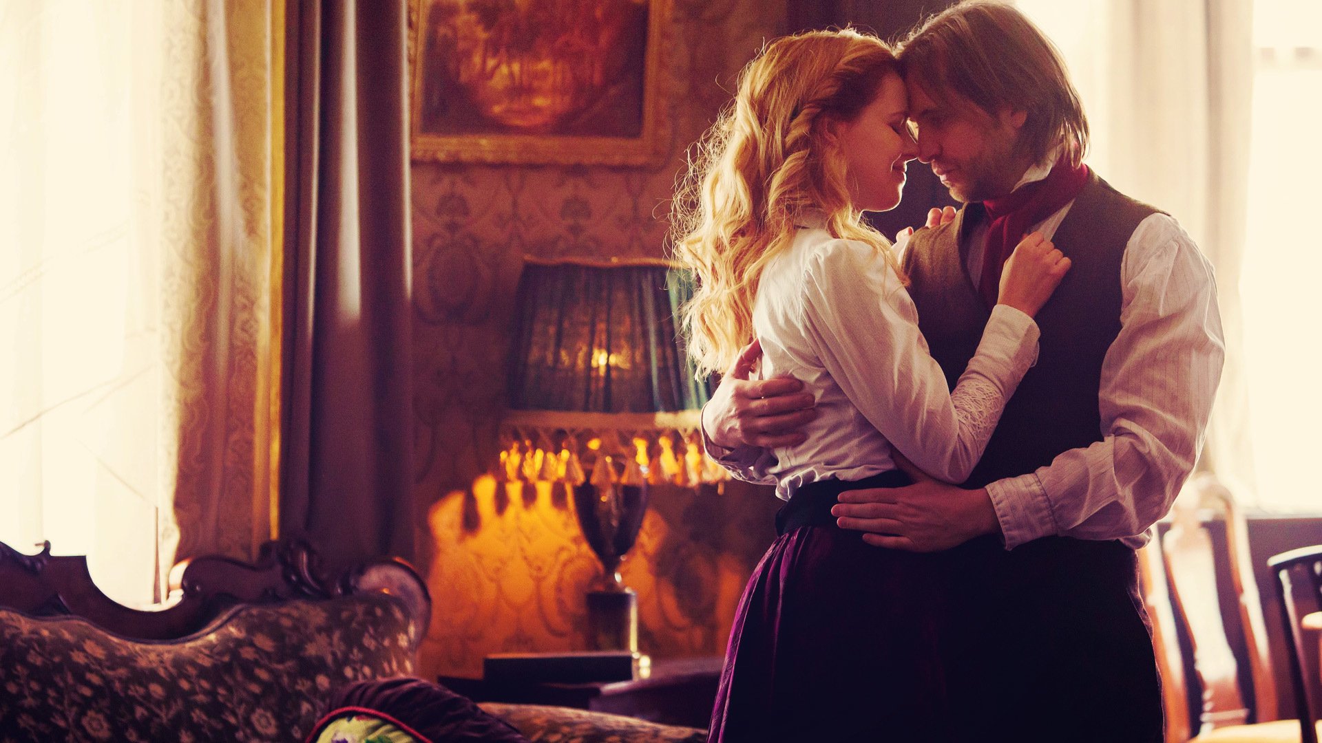 HD PC desktop wallpaper of the TV show 12 Monkeys: two characters embrace in a warmly lit, vintage parlor, an intimate, tense moment captured for a desktop background.