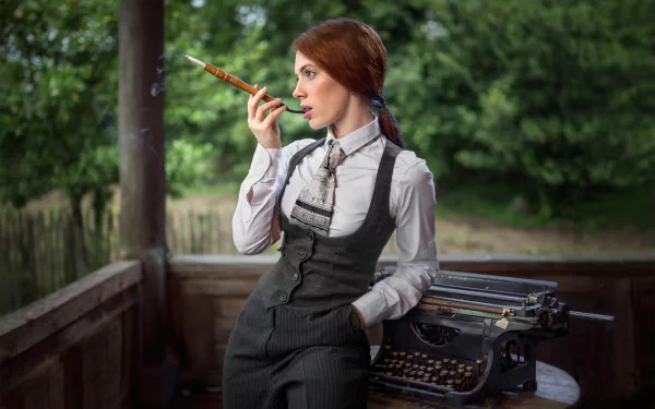 A red-haired woman smokes leisurely by an old typewriter in a rustic outdoor setting. The image features a depth of field effect, highlighting the model in an HD desktop wallpaper and background.
