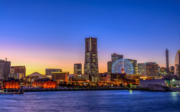 Sunset view of Yokohama city skyline featuring skyscrapers, a ferris wheel, and waterfront buildings under a clear sky.