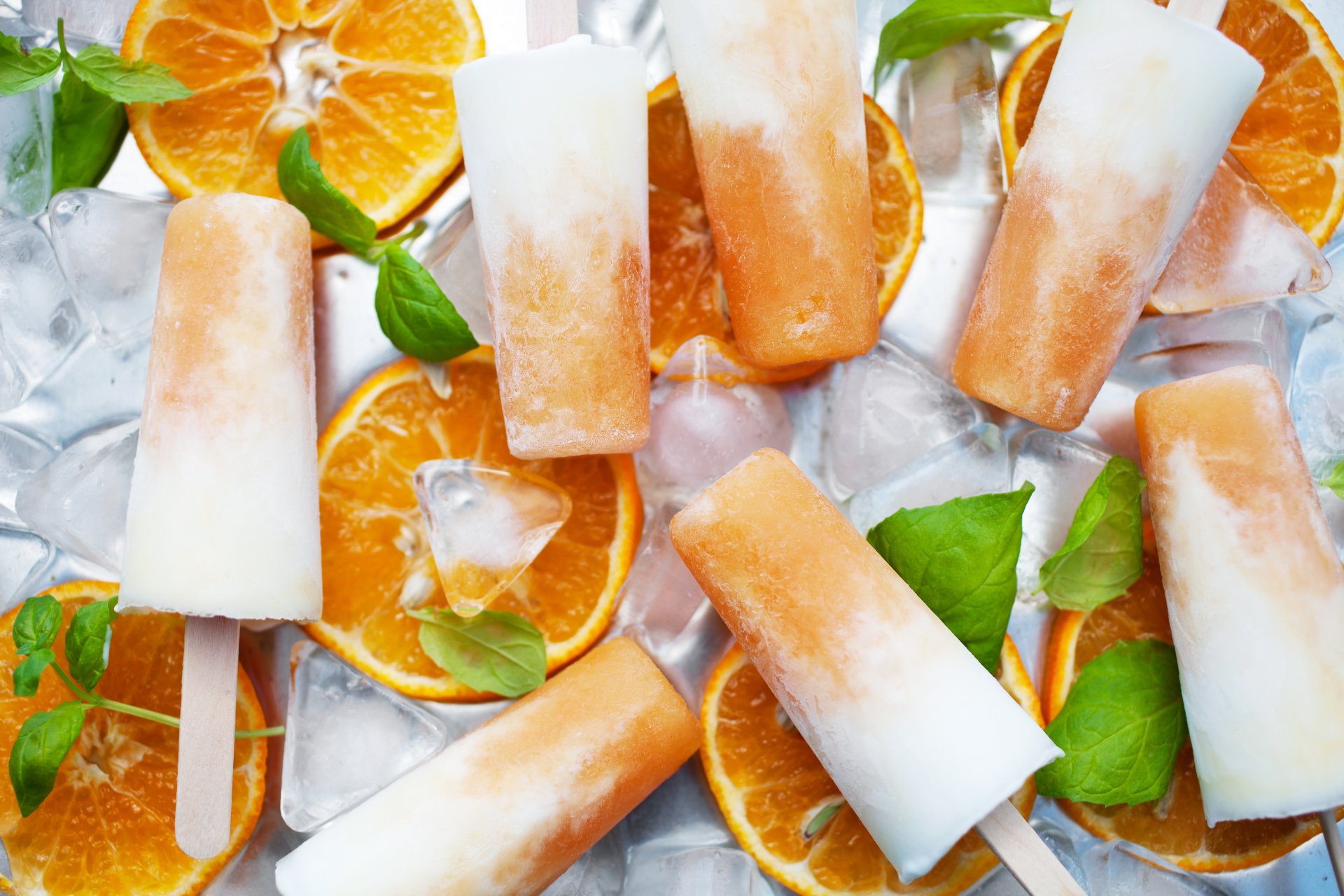4K Ultra HD wallpaper featuring orange and cream ice cream popsicles surrounded by ice cubes and fresh orange slices, highlighting vibrant fruit and sweet treats.