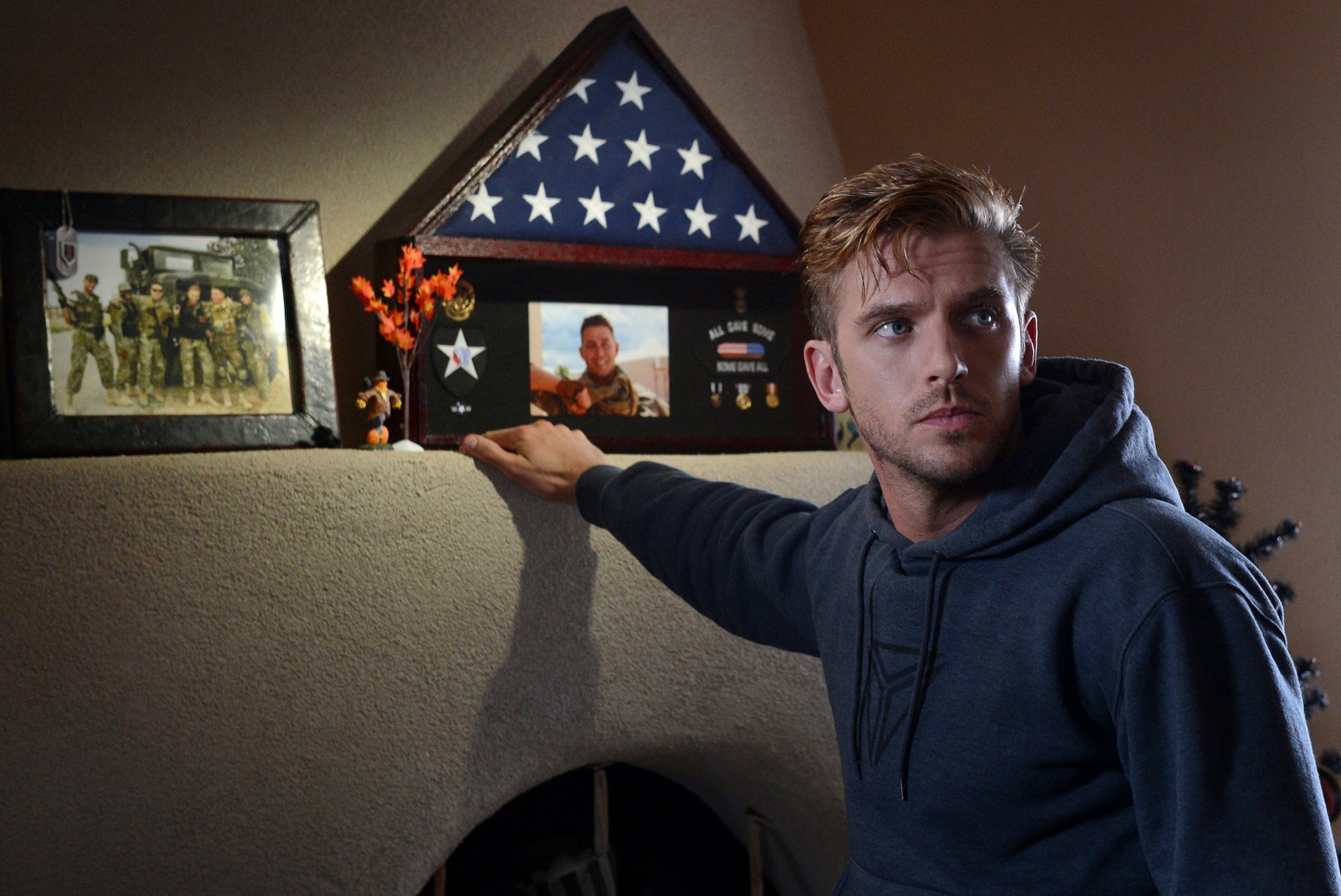 HD desktop wallpaper featuring Dan Stevens with a contemplative expression, next to a shelf with military memorabilia.