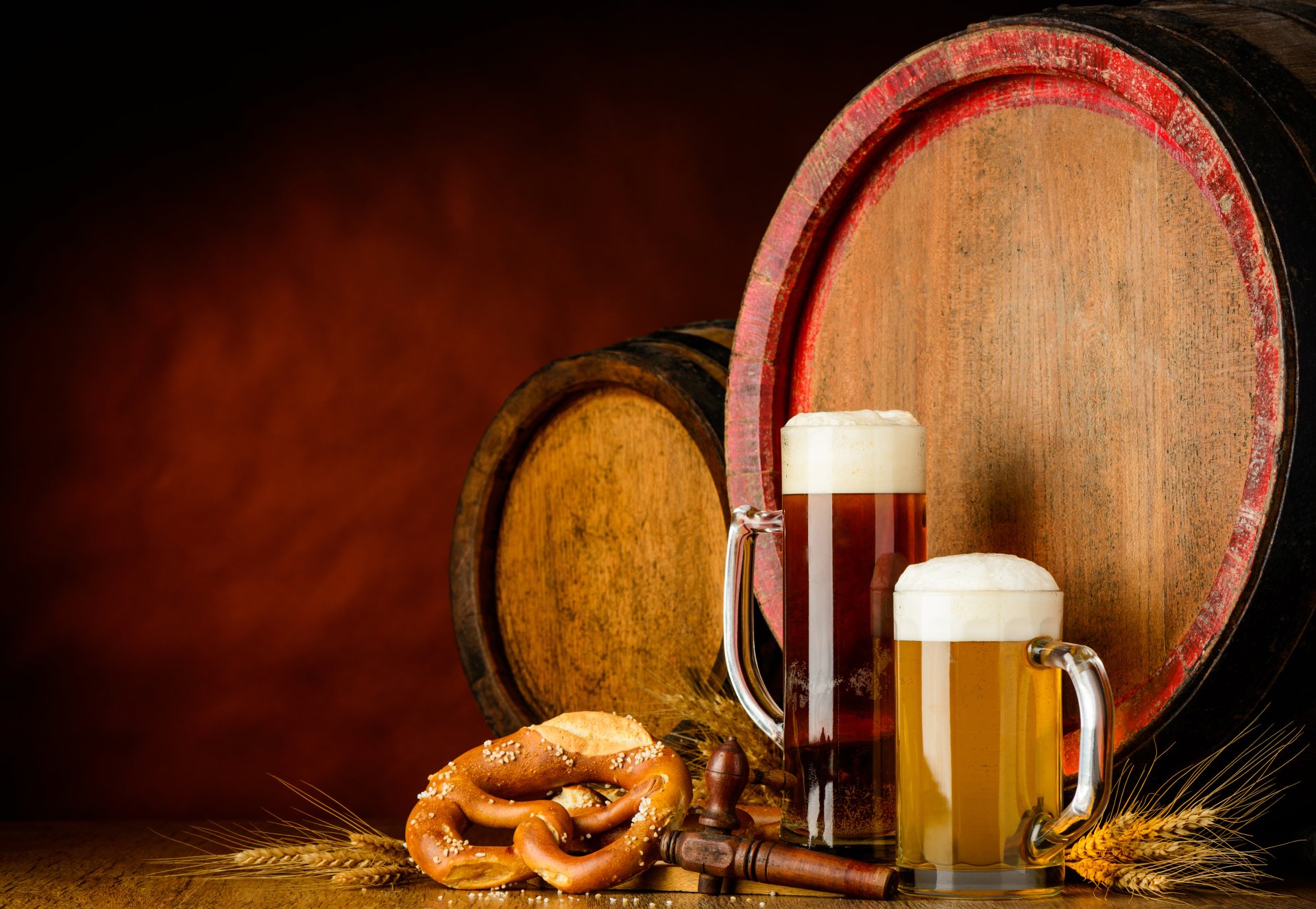 4K Ultra HD still life wallpaper featuring wooden barrels, two glasses of beer, a pretzel, and scattered barley on a warm brown background.