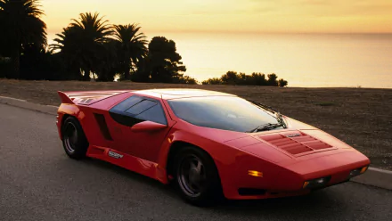 HD PC desktop wallpaper: red Vector W8 vehicle, a wedge-shaped sports car, parked on a coastal road at sunset with palm trees and the ocean in the background.