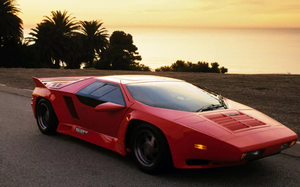 HD PC desktop wallpaper: red Vector W8 vehicle, a wedge-shaped sports car, parked on a coastal road at sunset with palm trees and the ocean in the background.